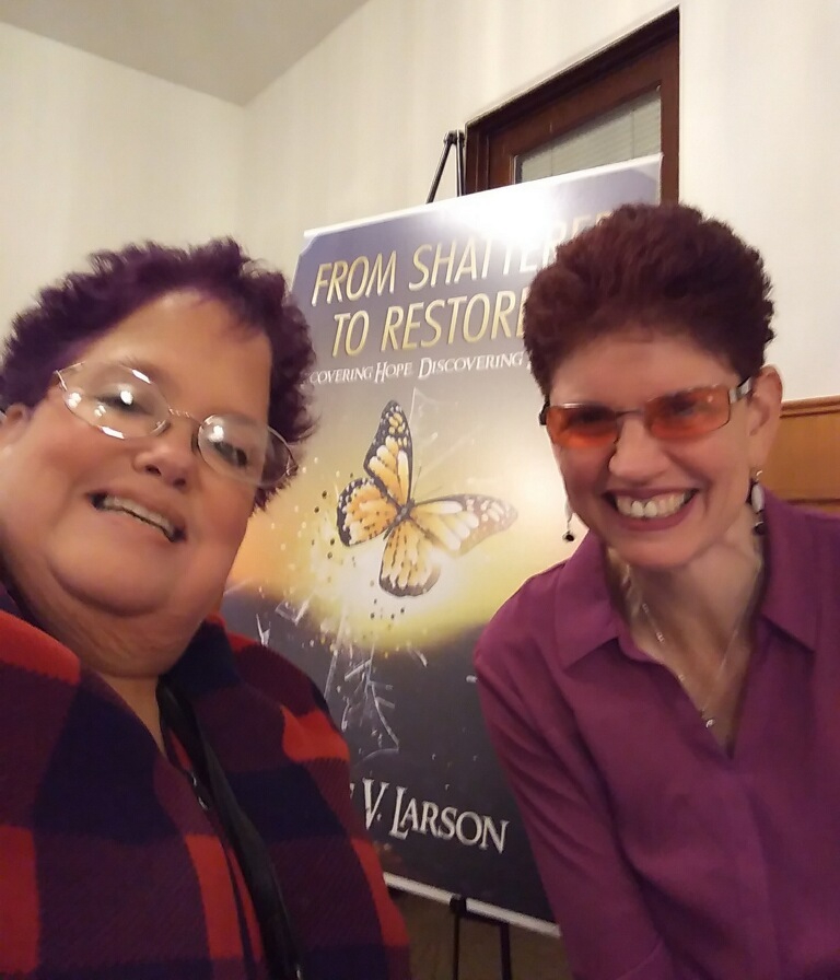 Nannette V. Larson and friend standing in front of Book cover poster